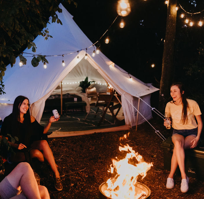 camp fire in front of bell tent with people in camp chairs